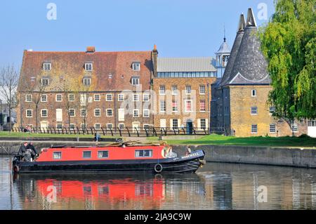 Crew men & red narrow boat on canalised River Lea Navigation at historical Grade I listed buildings on Three Mills site Bromley By Bow East London UK Stock Photo
