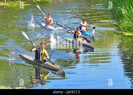 Summer view looking down from above on a group of four enthusiastic young males  paddling kayaks on calm River Chelmar in Chelmsford Essex England UK Stock Photo