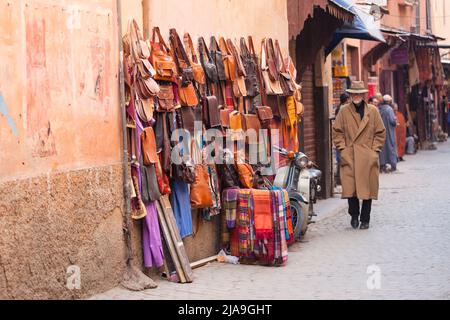 Man in hat and coat walking in Souk, Marrakech, Morroco. Leather goods for sale in the Old Medina Stock Photo