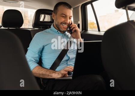 Businessman using laptop talking on smartphone while going by car Stock Photo