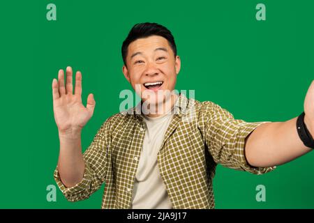 Hello. Happy asian middle aged man taking selfie and waving hand at camera, having online video call Stock Photo