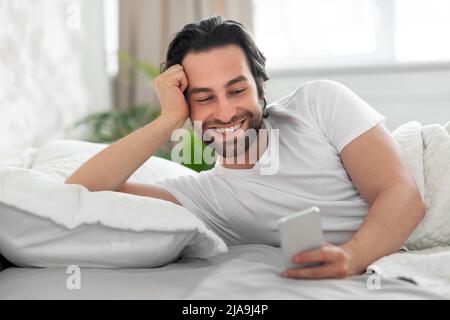 Happy millennial man using cell phone after waking up Stock Photo