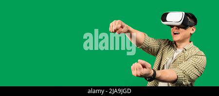 Emotional mature asian man playing video games, wearing VR glasses and gesturing, green background, free space Stock Photo