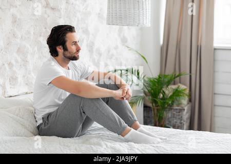 Side view of lonely young man sitting on bed alone Stock Photo