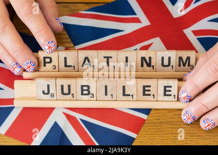 Woman's fingers with fingernails painted with the Union Jack holding scrabble letters that spell out Platinum Jubilee - Queen's Elizabeth June 2022 Stock Photo