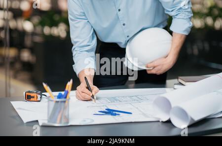 Cropped millennial middle eastern engineer with hard hat works with drawings at workplace in office Stock Photo