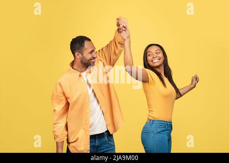 Affectionate black couple dancing, turning and spinning over yellow studio background Stock Photo