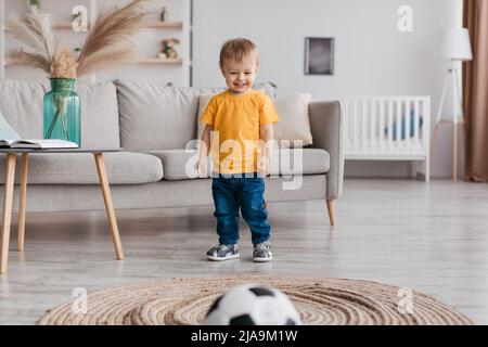 Portrait of adorable toddler boy football fan playing soccer ball and smiling, having fun at home in living room Stock Photo