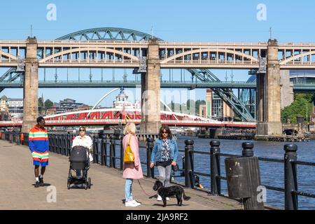 People enjoy a walk on the Quayside in Newcastle upon Tyne, UK, on a beautiful blue sky day, with bridges in the background. Stock Photo