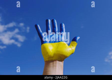 Close up shot of a man's hand lit by sunshine painted in colors of Ukrainian national flag. .A hand raised over blue sky background as a symbol of sup Stock Photo