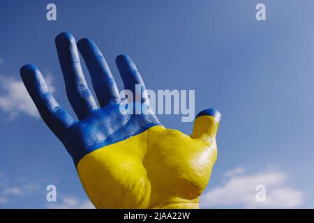 Close up shot of a man's hand lit by sunshine painted in colors of Ukrainian national flag. .A hand raised over blue sky background as a symbol of sup Stock Photo