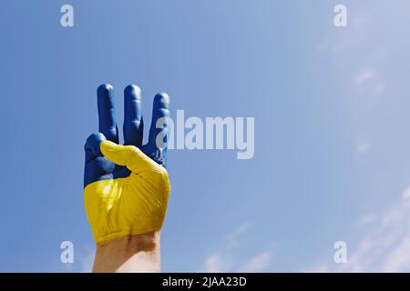 Man's hand lit by sunshine painted in colors of Ukrainian national flag showing a traditional trident hand gesture as a symbol of support and solidari Stock Photo