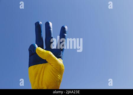 Man's hand lit by sunshine painted in colors of Ukrainian national flag showing a traditional trident hand gesture as a symbol of support and solidari Stock Photo