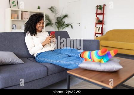 Millennial african american woman using mobile phone sitting on couch at home Stock Photo