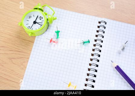 Close up of notepad with colored pencil, clips and alarm clock on a table Stock Photo