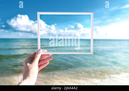 White frame in female hand. Summer sea and blue sky background. Mock up Stock Photo