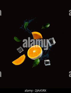 Creative layout made of fresh orange fruit, ice, leaves and water splash. Vitamins, healthy diet food idea. Minimal flying summer concept on black bac Stock Photo