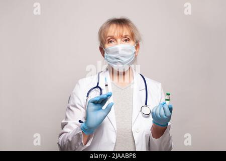 Senior woman doctor holding syringe and vaccine. Prevention, immunization, medicine and treatment concept Stock Photo