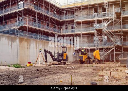 Builder driving dumper truck and excavator on new building construction site. Surveying equipment on construction site Stock Photo