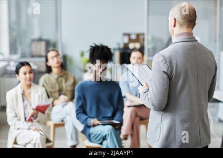 Back view of mature male coach giving lecture or seminar in office to diverse group of people, copy space Stock Photo