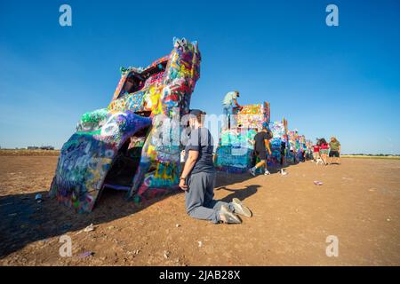 Cadillac Ranch, an art installation near Amarillo, TX, USA. An artist sprays paint on one of the cars. Route 66 Stock Photo