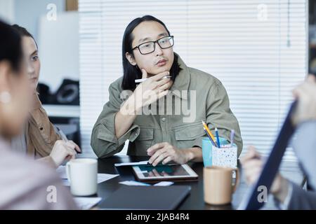 Portrait of pensive Asian man in business meeting with group of people discussing project in office Stock Photo