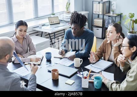 High angle view at diverse group of people at meeting table in office setting discussing projects Stock Photo