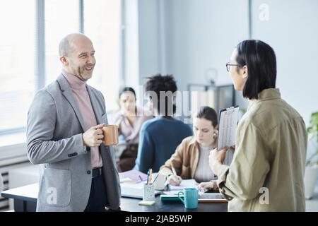 Side view portrait of two business people chatting and smiling during break at educational seminar in office Stock Photo