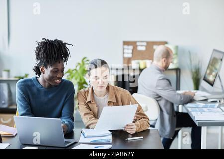Portrait of two young business people using laptop and reading documents while working on project in office Stock Photo