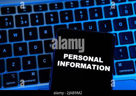 PERSONAL INFORMATION phrase seen on a smartphone placed on a blue lit blurred laptop behind it. Concept. Stock Photo