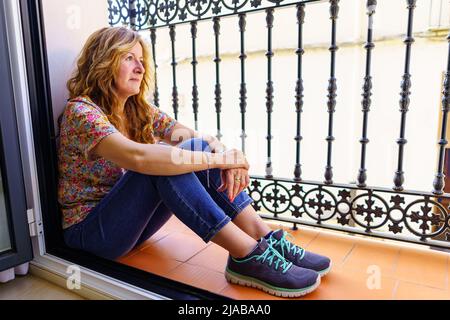 Mature white woman sitting on the balcony floor of her house in a relaxed and calm way. Stock Photo