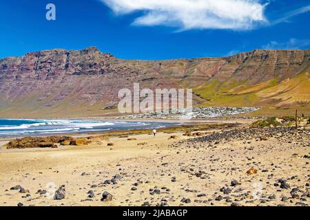 Beautiful wild rough lagoon, secluded white village located at the bottom of a rock face, sand beach, ocean waves  - Playa de Sotavento Jandia, Risco Stock Photo