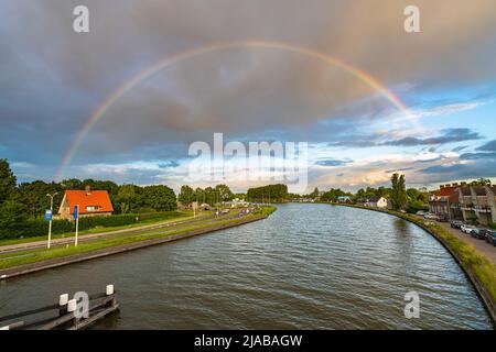 Bright colorful rainbow over channelized river Gouwe near the town of Gouda, Netherlands Stock Photo