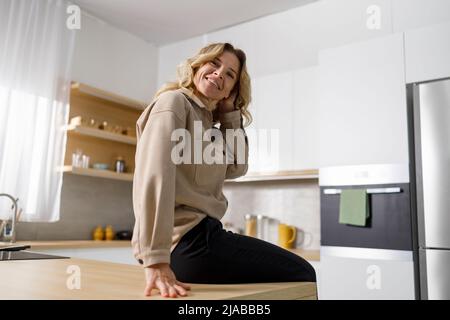 Pretty middle aged housewife sitting on the kitchen table Stock Photo
