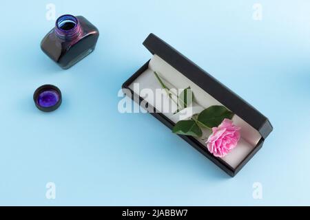 Vintage set of fountain pen, inkpot and blooming pink rose on blue background. Romantic minimal concept. Valentines Day creative card. Flat lay. Stock Photo