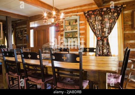 Antique table, high back chairs and furnishings in dining room inside old circa 1825 Canadiana cottage style log home. Stock Photo