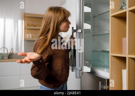 Young woman looking in empty fridge. My fridge is empty. Where is the food? Stock Photo