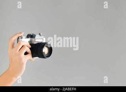 Old photo camera in woman hand on grey background with vintage color effect. Minimal retro style. Copy space. Stock Photo