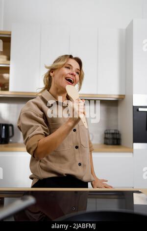 Portrait of a middle-aged woman singing while cooking in the kitchen at home Stock Photo