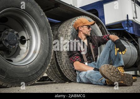 https://l450v.alamy.com/450v/2jabmcg/semi-truck-driver-resting-next-to-his-truck-seating-on-a-ground-heavy-duty-transportation-job-theme-2jabmcg.jpg