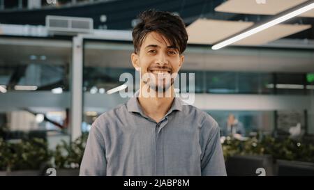 Happy indian bearded handsome adult man stand in hall office smiling looking at camera cheerful male arab brunette guy businessman entrepreneur Stock Photo