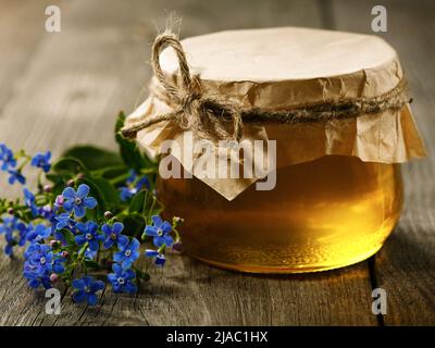 Glass jar with honey and spring flowers on an old wooden table Stock Photo