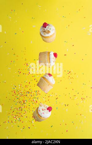 Creative composition. On a bright yellow background with multi-colored confetti, muffins with cream and raspberries in a frozen flight. Advertisement, Stock Photo