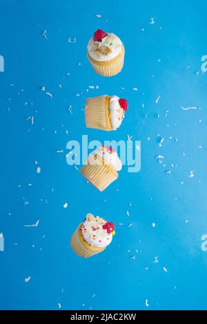 Muffins with cream and raspberries in a frozen flight on a bright blue background with white confetti. Children, youth culture, birthday. Restaurant, Stock Photo