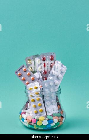 Medical pills and blisters in glass jar on turquoise background. Space for text. Stock Photo
