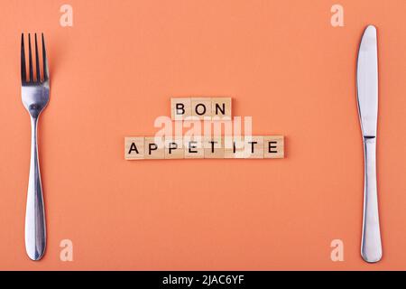 Wooden blocks with inscription Bon appetit and cutlery on color background. Table serving. Stock Photo