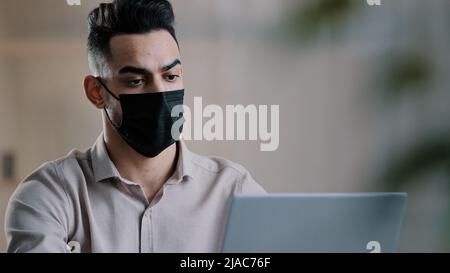 Arabian sick businessman in medical mask designer programmer typing on laptop search information in network develop startup project chatting in online Stock Photo