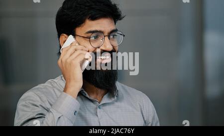 Smiling confident adult millennial man arabian businessman professional worker make business call talk on phone in office happy bearded guy salesman Stock Photo