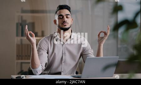 Calm arabian business man professional worker eyes closed taking break meditating on work desk ignoring stress breathing for peaceful mind male boss Stock Photo