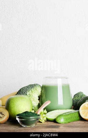 green smoothie in glass, spirulina powder, vegetables and fruits on wooden background. healthy, raw, vegan diet concept. copy space Stock Photo